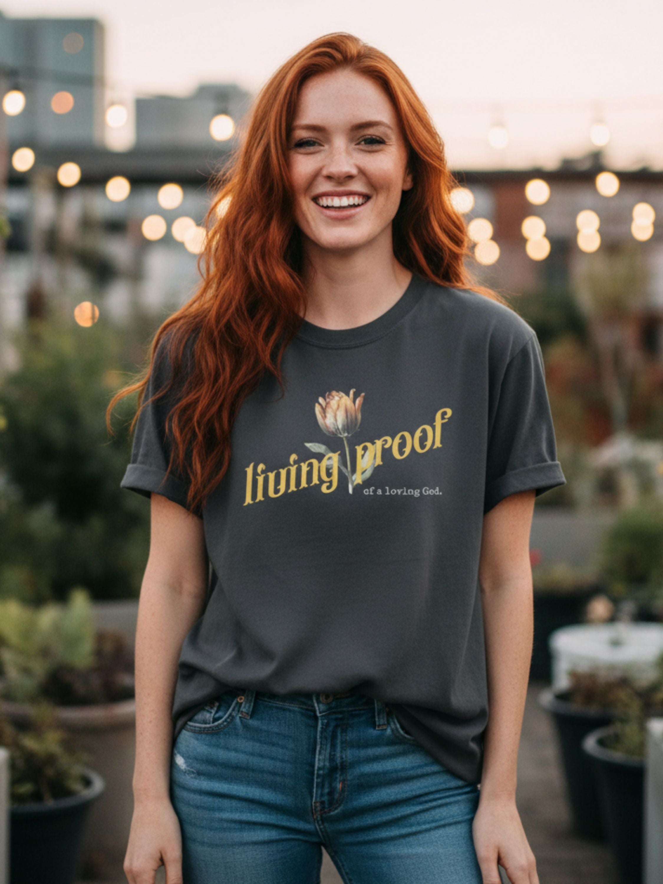 Woman wearing a 'living proof' t-shirt in an outdoor setting with plants and lights.